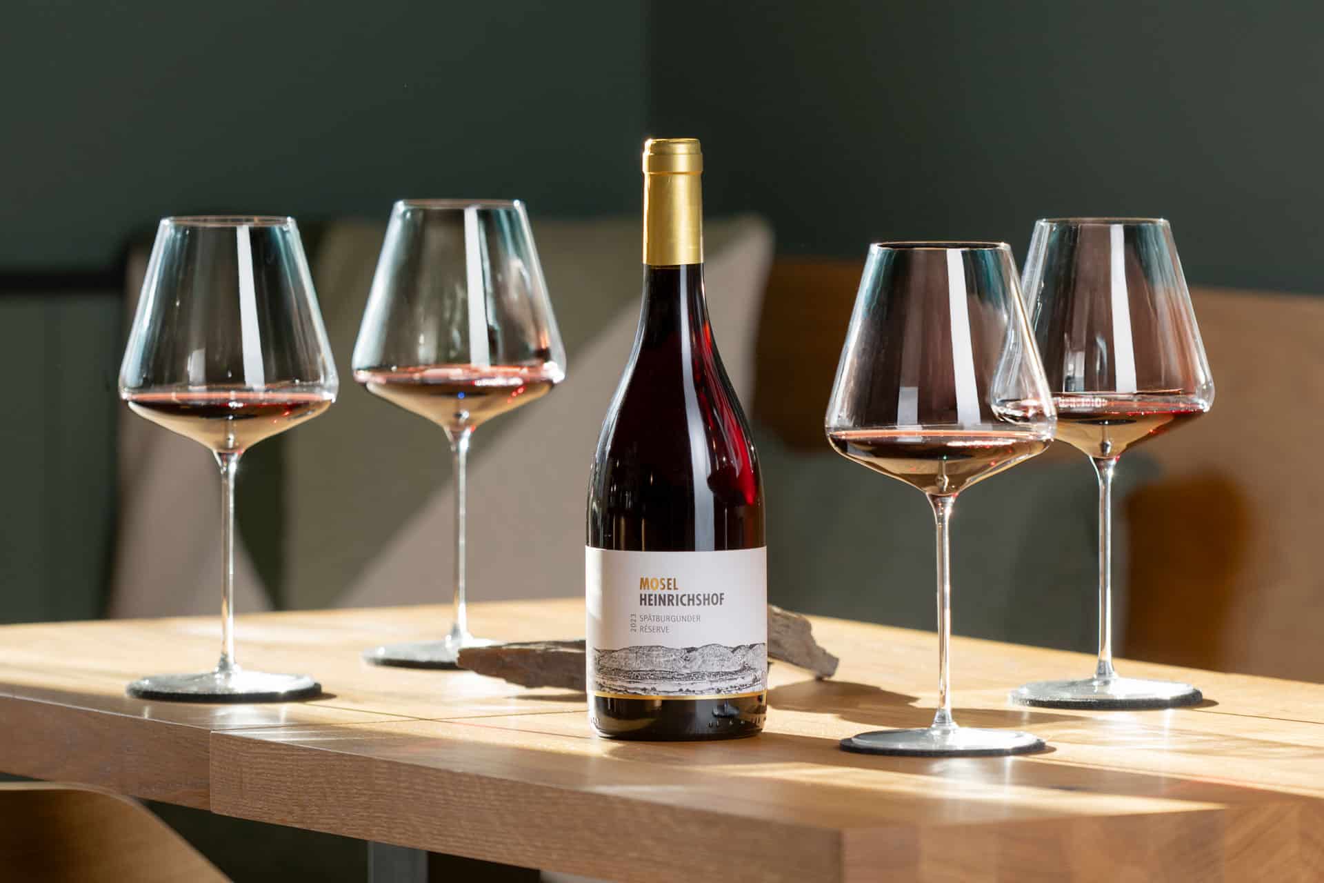 Flasche Spätburgunder Rotwein des Weinguts Heinrichshof umgeben von vier Rotweingläsern auf einem Holztisch Rotwein Flasche